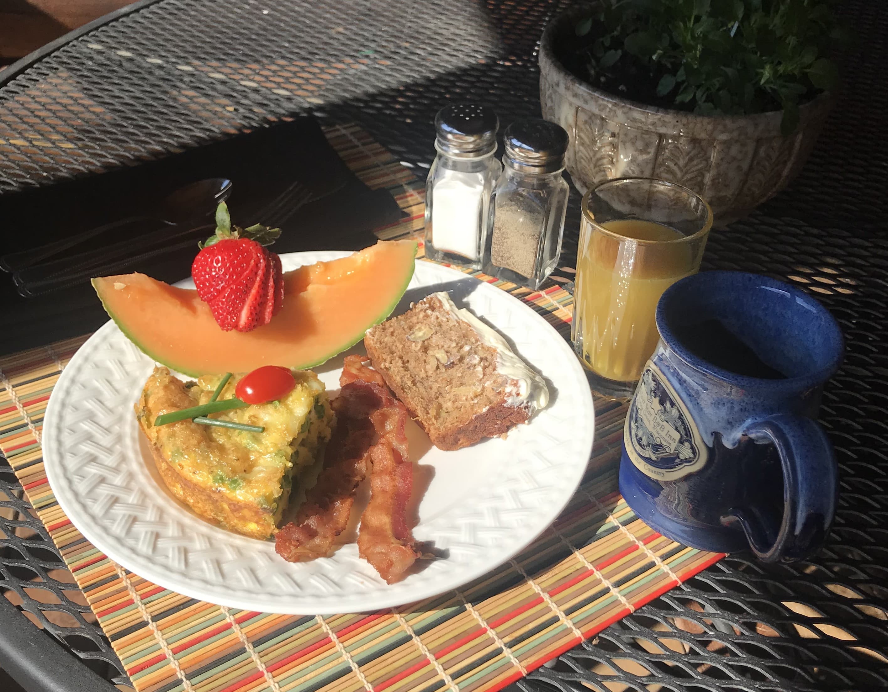 A plate of breakfast featuring an omelet, bacon, a slice of bread, and fruit, accompanied by a glass of orange juice and a mug of coffee.