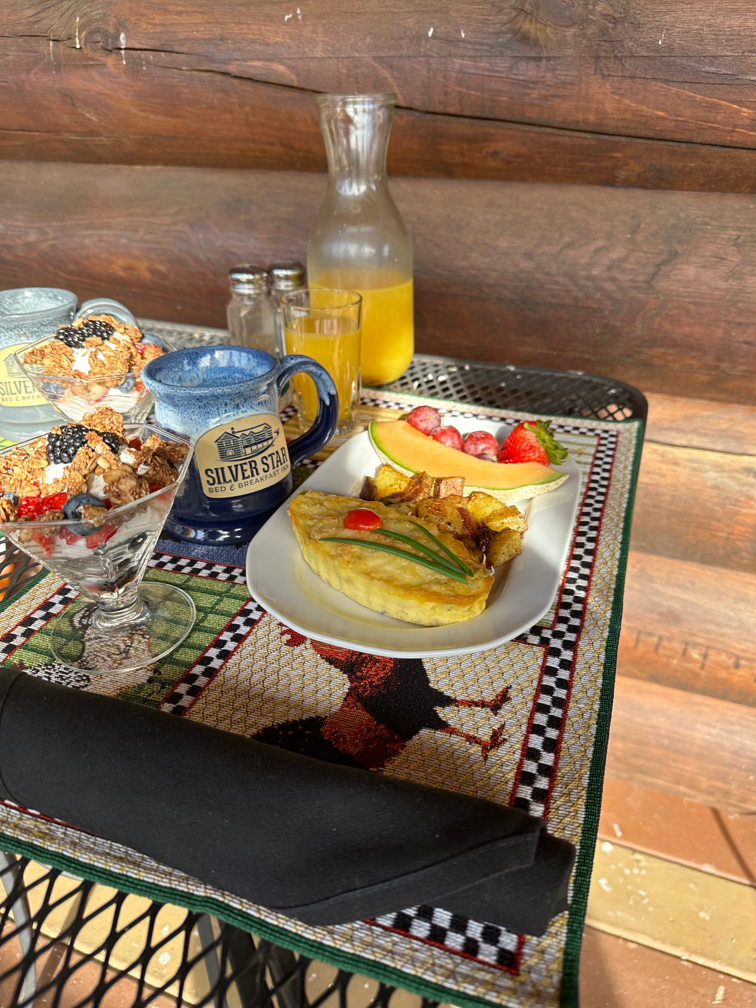 A beautifully arranged breakfast table featuring an omelette, roasted potatoes, fresh fruit, cereal, and a drink, set against a rustic wooden backdrop.