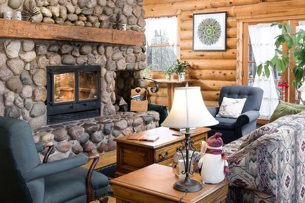 Cozy log cabin living room with a stone fireplace, comfortable seating, and warm decor.