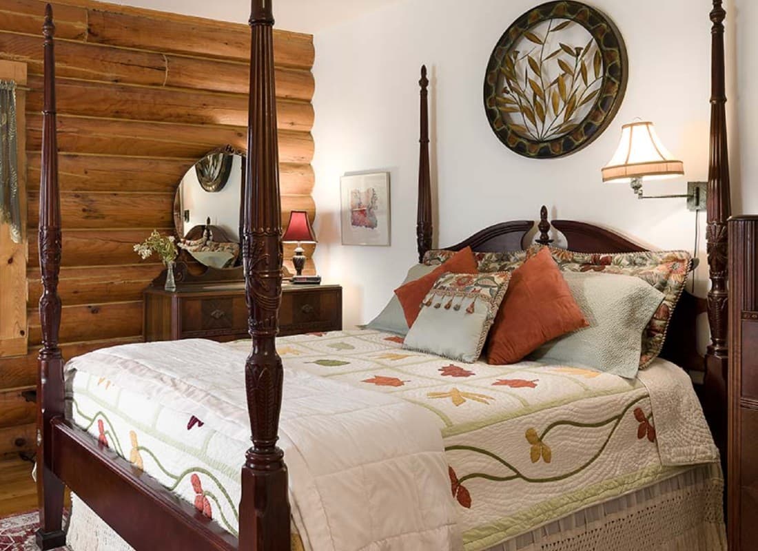 A cozy bedroom featuring a wooden four-poster bed, decorative pillows, and a rustic log wall.
