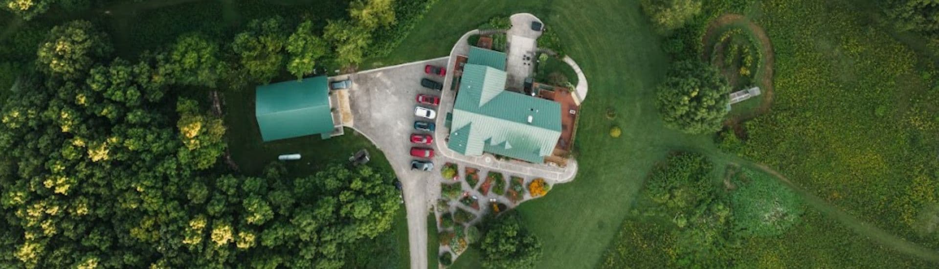 Aerial view of a modern building surrounded by lush greenery and a parking area.