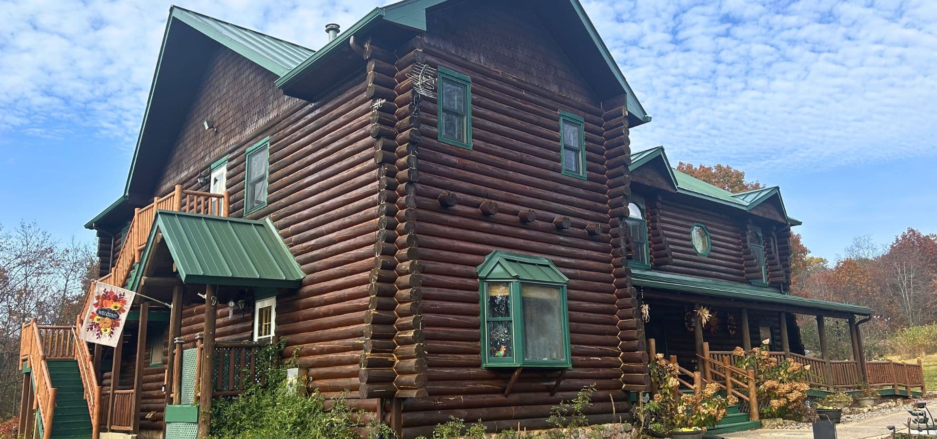 A rustic log cabin with a green roof and surrounding foliage.